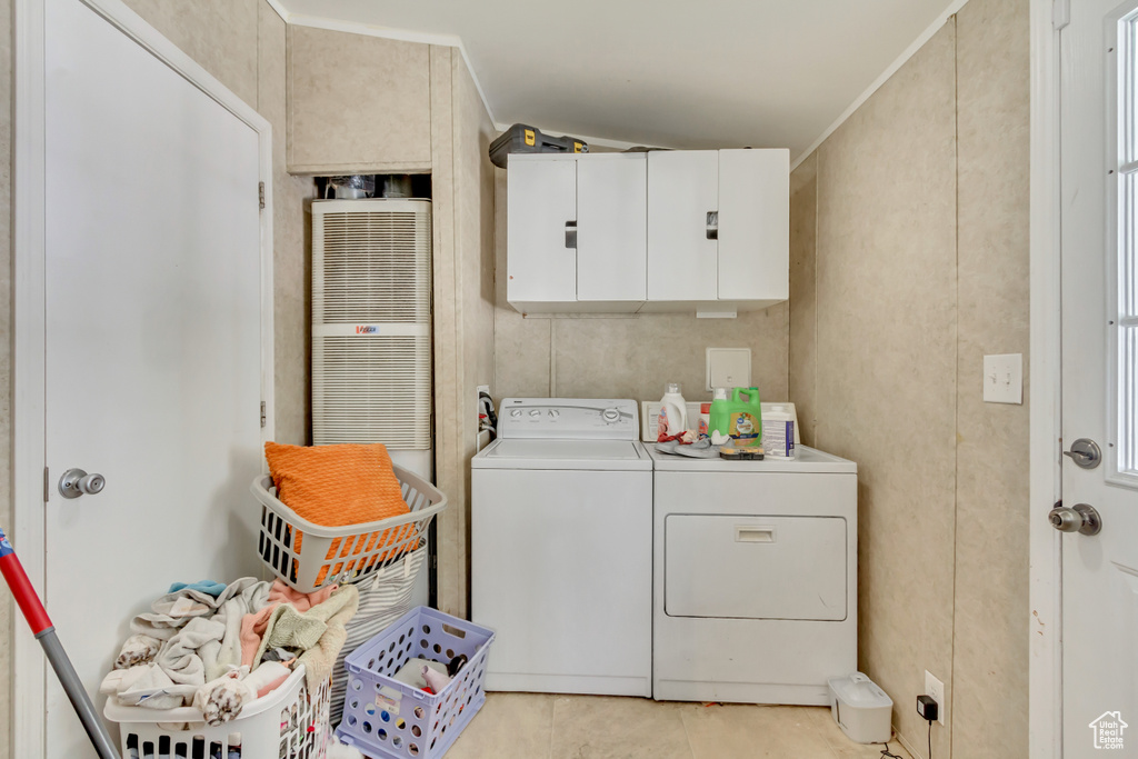 Washroom with light tile patterned floors, washer and dryer, cabinet space, ornamental molding, and a heating unit