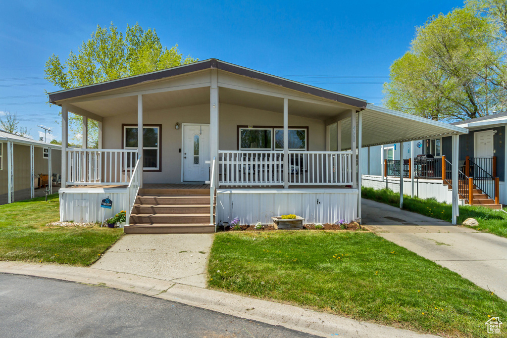 Manufactured / mobile home featuring a front lawn, stairway, covered porch, a carport, and concrete driveway