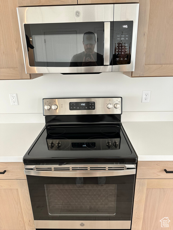 Kitchen with appliances with stainless steel finishes, light countertops, light brown cabinetry, and baseboards