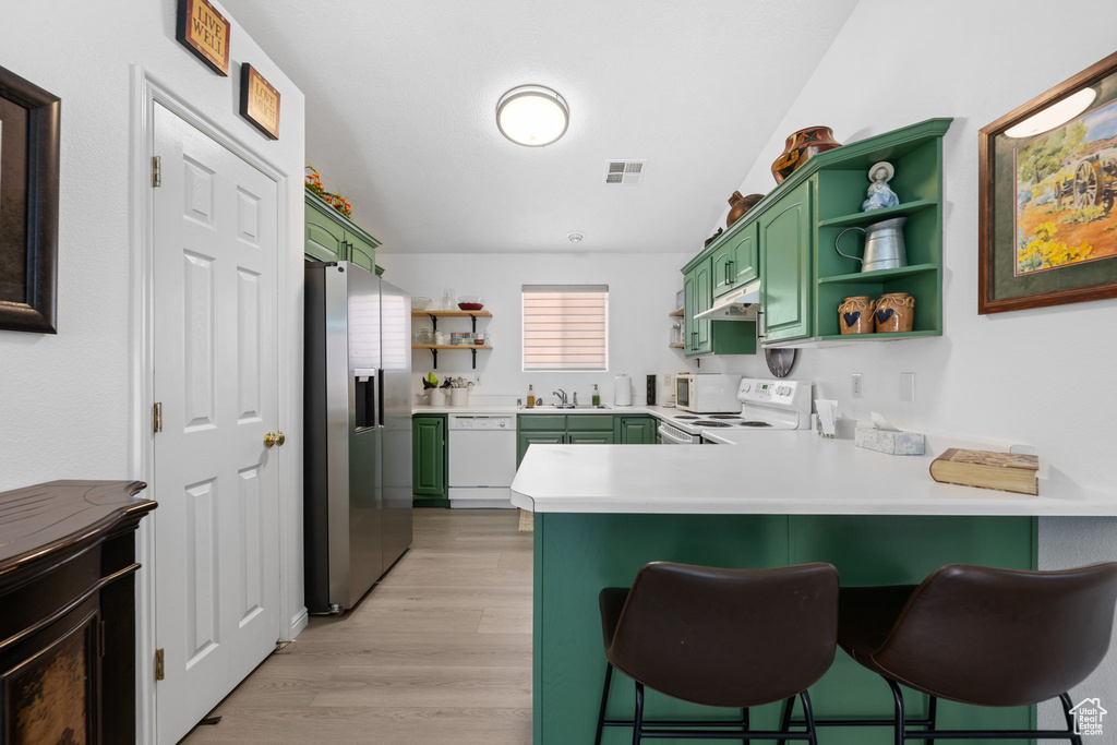 Kitchen with a peninsula, green cabinets, open shelves, and white appliances
