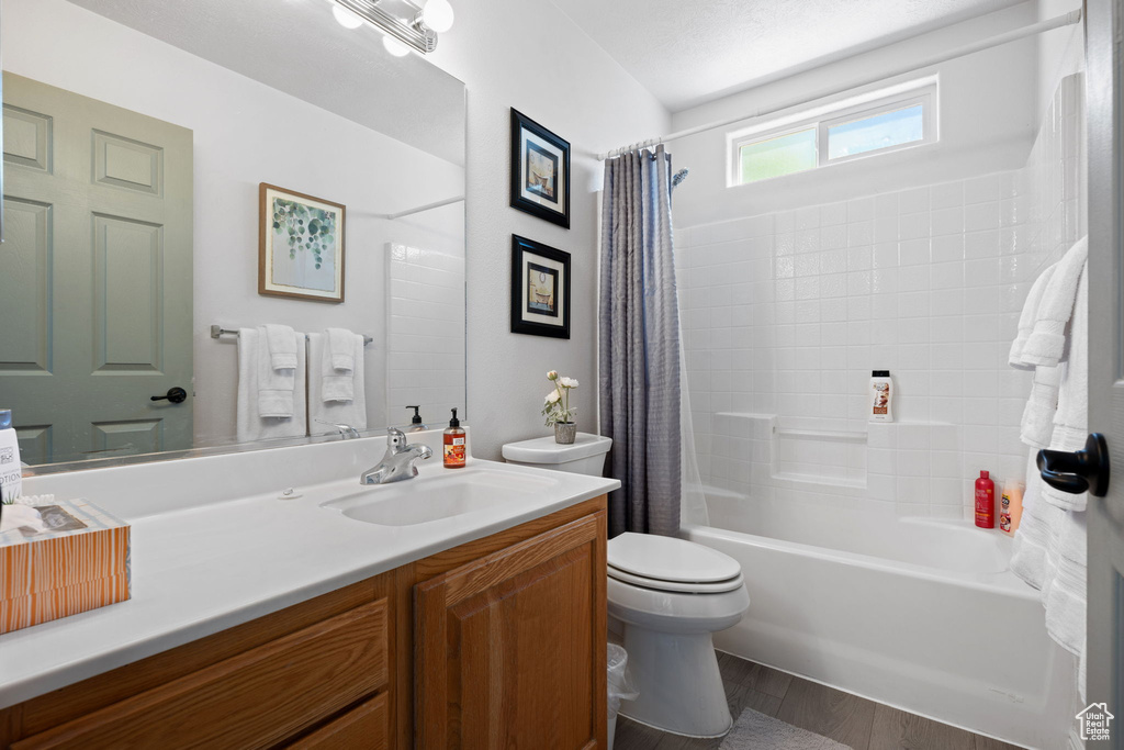 Bathroom with wood finished floors, shower / tub combo with curtain, toilet, and vanity