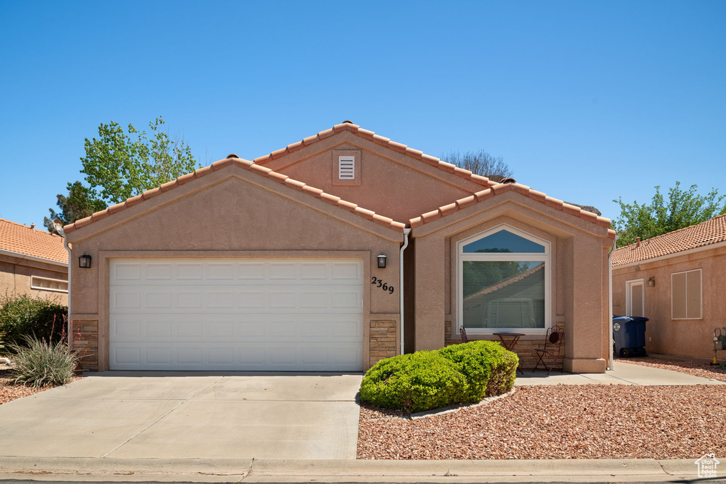 Ranch-style house featuring driveway, stone siding, a tiled roof, stucco siding, and a garage