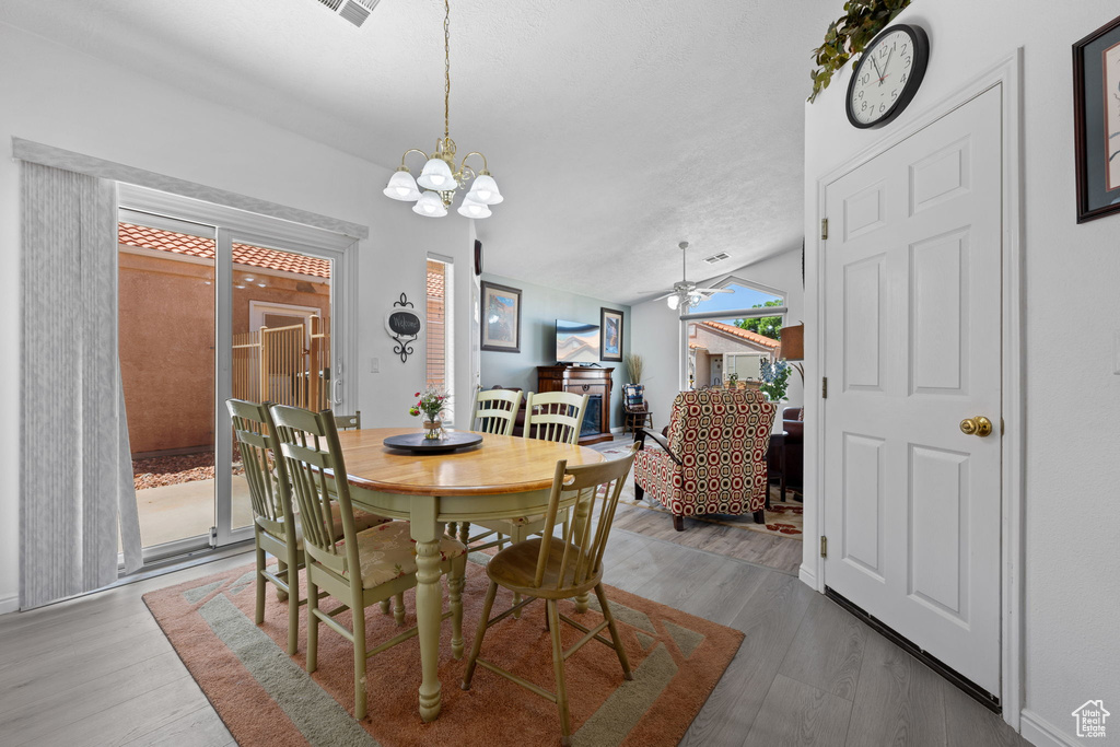 Dining room with lofted ceiling, wood finished floors, and ceiling fan with notable chandelier