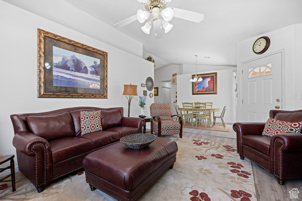 Living area featuring lofted ceiling, light wood-style floors, and ceiling fan with notable chandelier