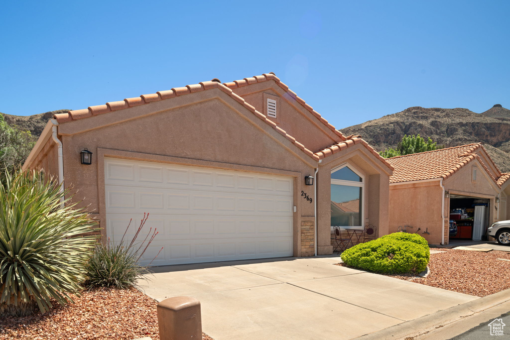 View of front of house with concrete driveway, a tile roof, a mountain view, stucco siding, and a garage