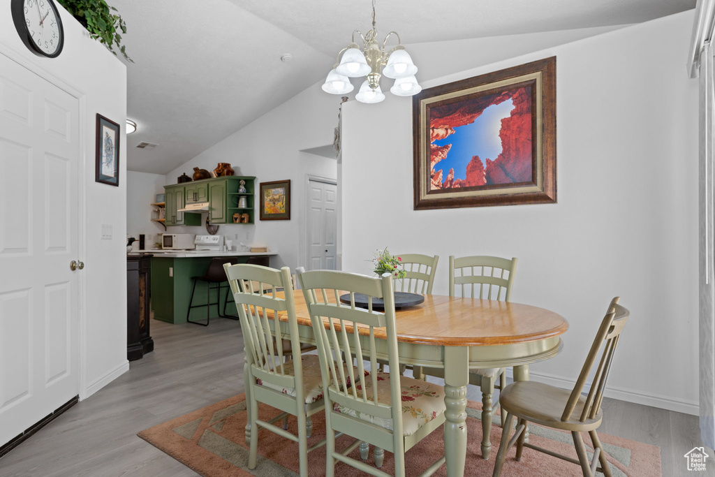 Dining area featuring a chandelier, light wood-style flooring, lofted ceiling, and baseboards