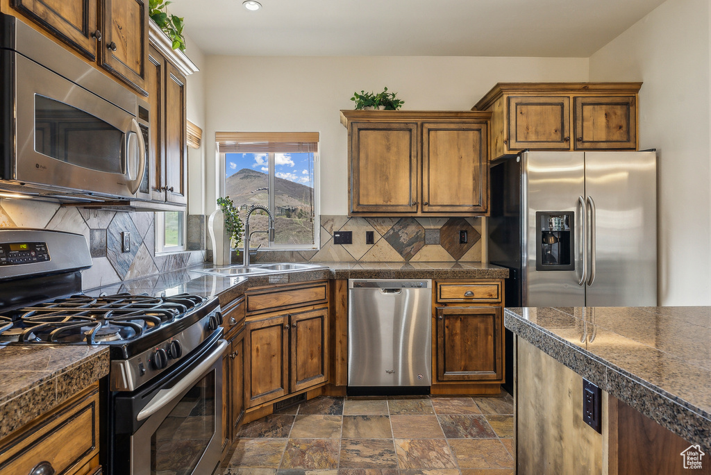 Kitchen with stainless steel appliances, tile counters, stone finish flooring, backsplash, and a sink