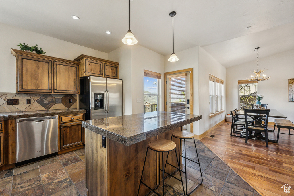 Kitchen with tile counters, a notable chandelier, a breakfast bar, vaulted ceiling, and appliances with stainless steel finishes