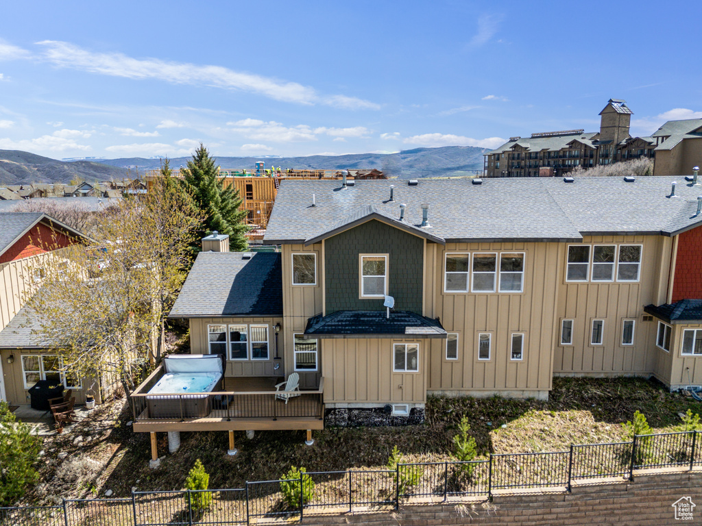 Rear view of house featuring board and batten siding, a deck with mountain view, a chimney, a shingled roof, and fence