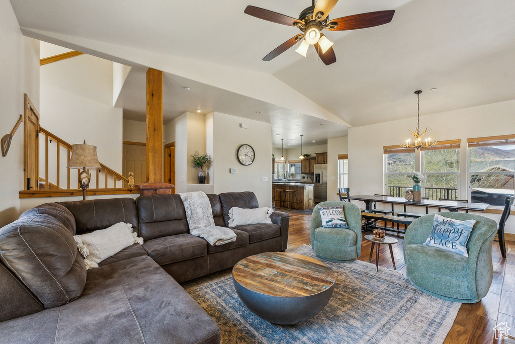 Living room with lofted ceiling, a wealth of natural light, wood finished floors, and ceiling fan with notable chandelier
