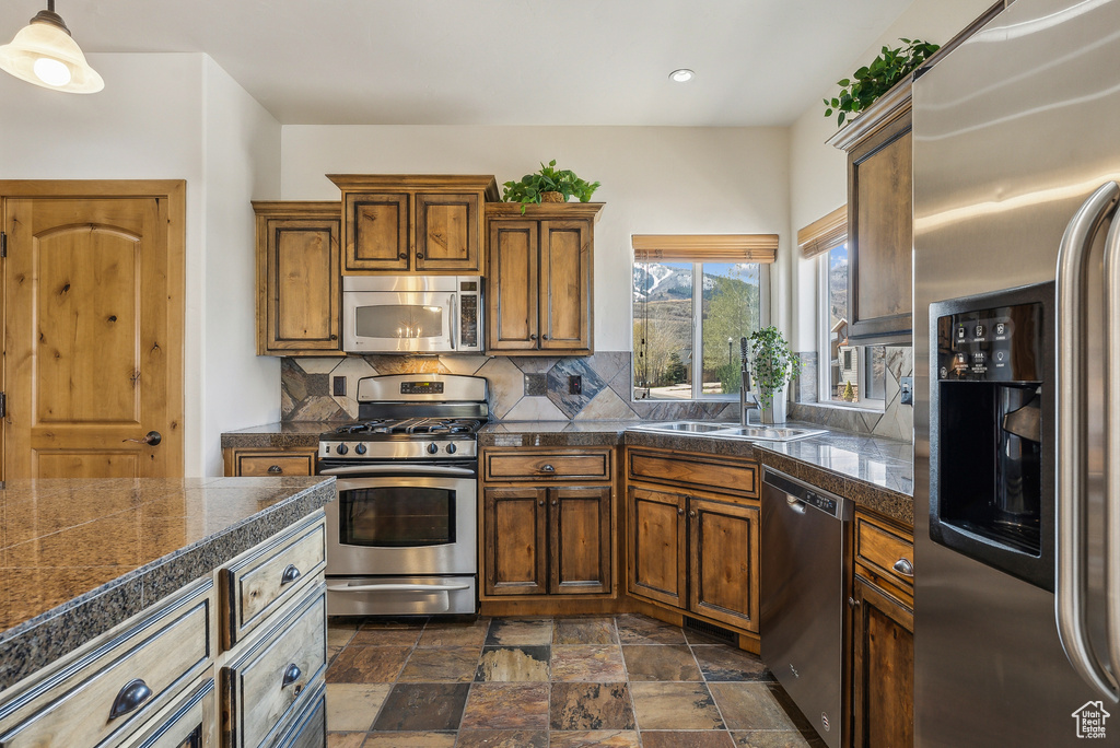 Kitchen featuring decorative backsplash, brown cabinetry, stainless steel appliances, a sink, and tile countertops