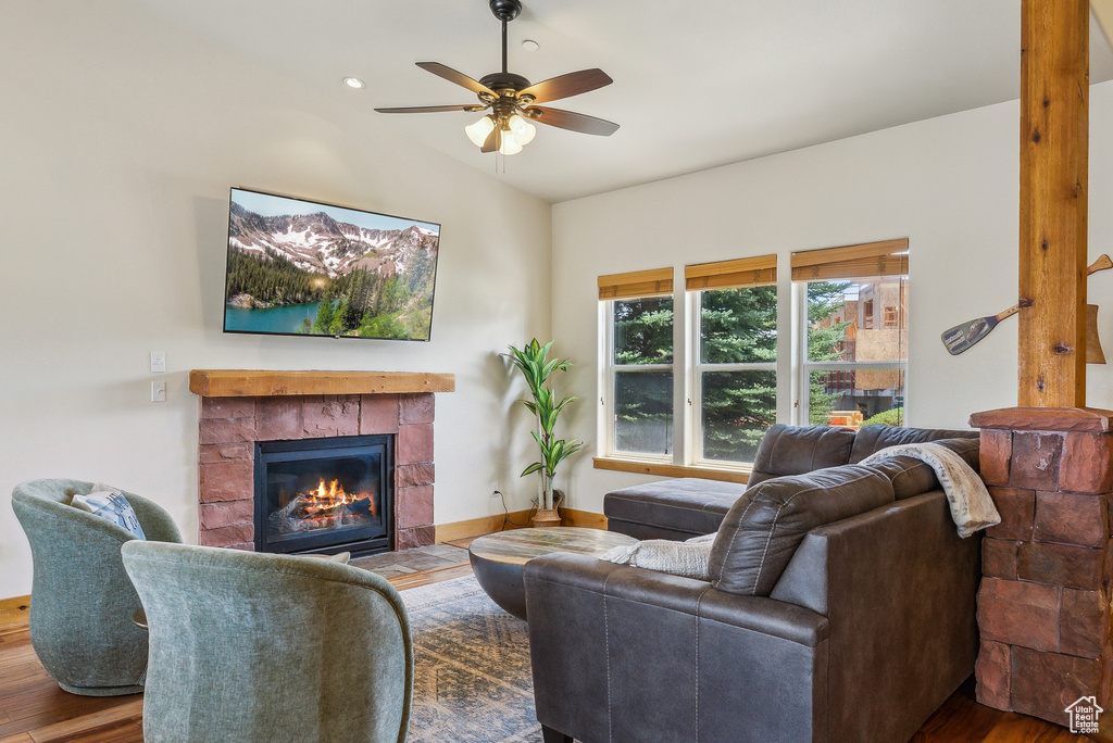 Living area with lofted ceiling, ceiling fan, a tiled fireplace, and wood finished floors