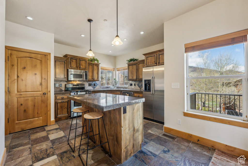 Kitchen featuring stone tile flooring, stainless steel appliances, a breakfast bar, tile countertops, and baseboards