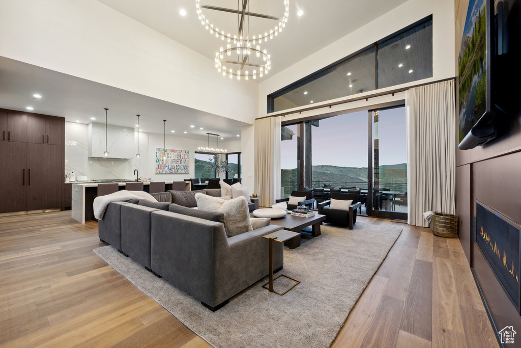 Living room featuring light wood-style flooring, a large fireplace, an inviting chandelier, recessed lighting, and a high ceiling