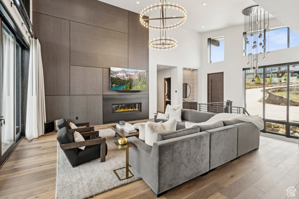 Living room featuring recessed lighting, a chandelier, light wood finished floors, a glass covered fireplace, and a towering ceiling