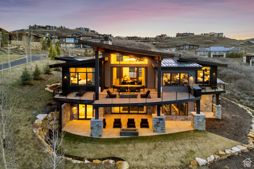 Back of property with a standing seam roof, a balcony, a patio, and stone siding