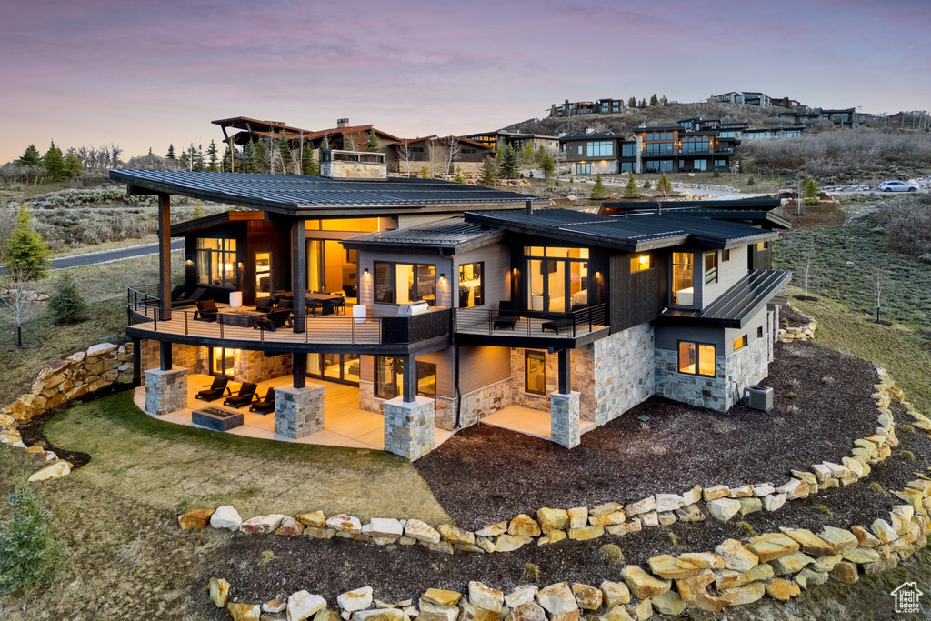 Back of property at dusk with a patio, a balcony, metal roof, and stone siding