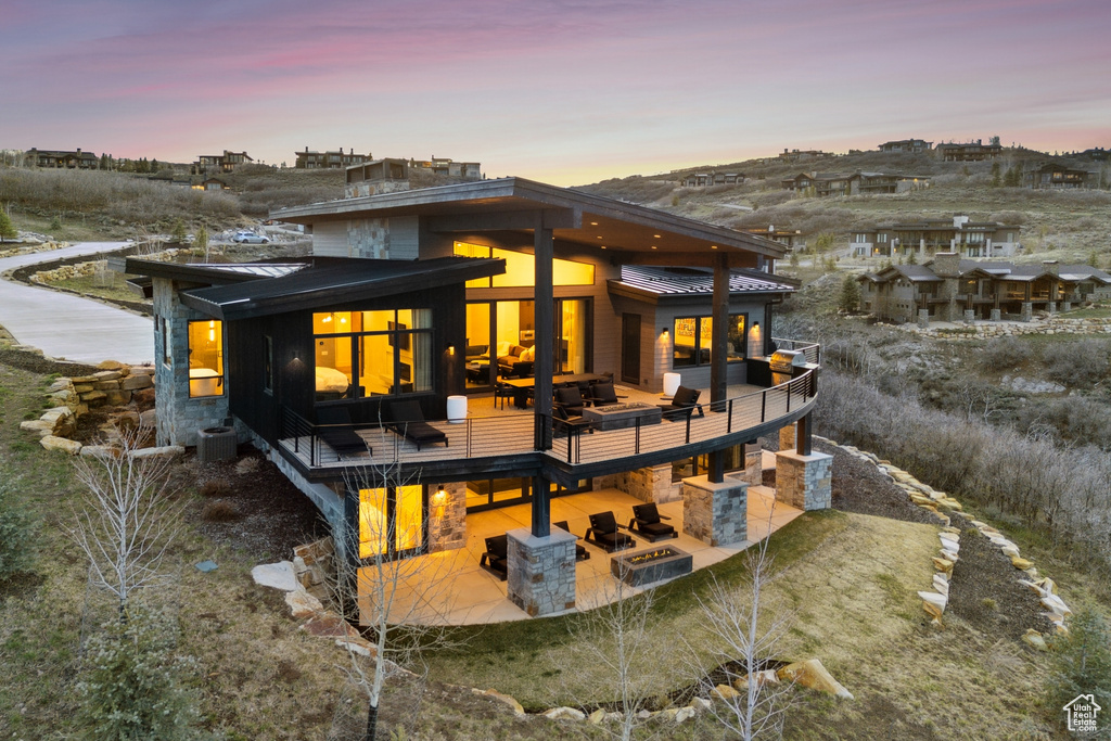 Back of house at dusk featuring a patio, a standing seam roof, cooling unit, and metal roof
