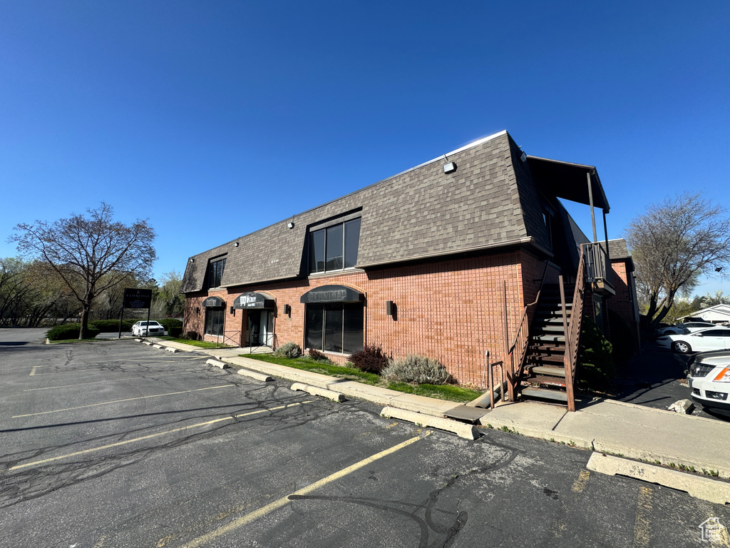 Exterior space featuring brick siding, a shingled roof, uncovered parking, and mansard roof