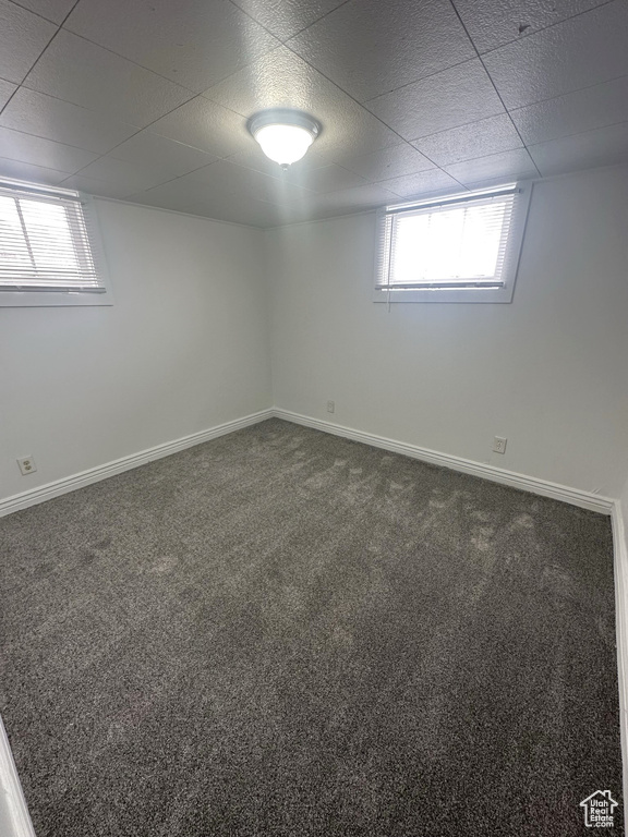 Below grade area with dark colored carpet, a wealth of natural light, and baseboards