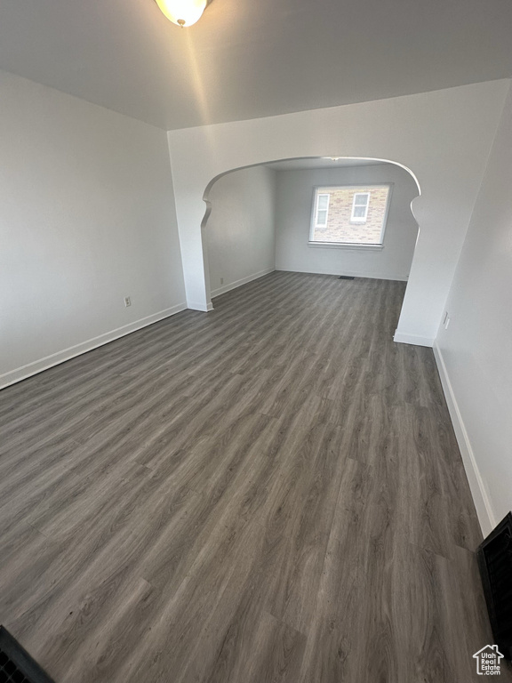 Additional living space featuring arched walkways, dark wood-style flooring, and baseboards