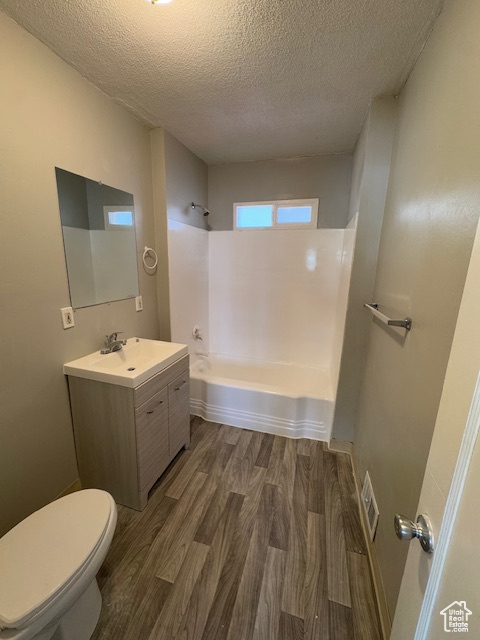 Full bathroom featuring wood finished floors, toilet, vanity, a textured ceiling, and bathtub / shower combination