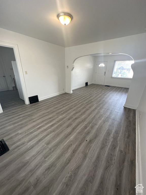 Unfurnished living room featuring arched walkways, baseboards, and dark wood-style flooring