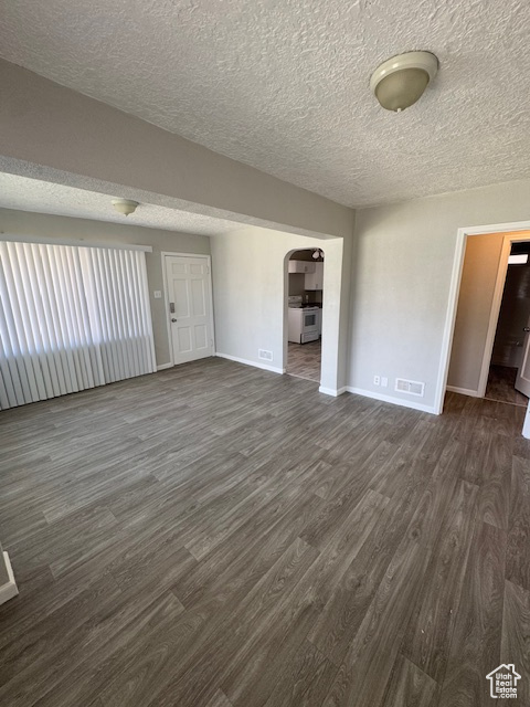 Unfurnished room featuring dark wood finished floors, visible vents, arched walkways, baseboards, and a textured ceiling