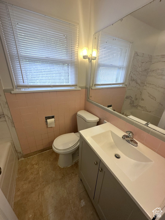 Full bath with a wealth of natural light, toilet, vanity, and tile walls
