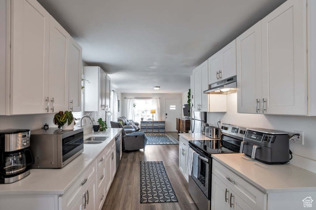 Kitchen featuring stainless steel appliances, under cabinet range hood, dark wood-style flooring, a sink, and open floor plan