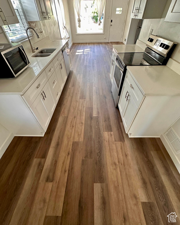 Kitchen featuring decorative backsplash, a sink, appliances with stainless steel finishes, light countertops, and dark wood-type flooring