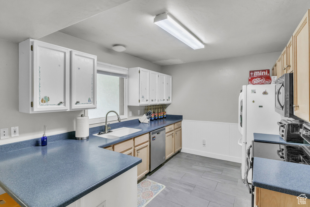 Kitchen with a sink, a peninsula, dark countertops, wainscoting, and appliances with stainless steel finishes