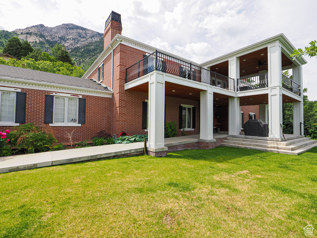 Back of property with a balcony, a yard, brick siding, a chimney, and a patio