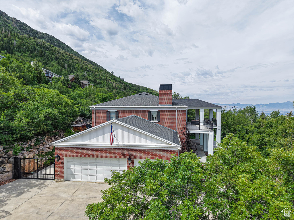 Rear view of house with a balcony, brick siding, a mountain view, a chimney, and driveway