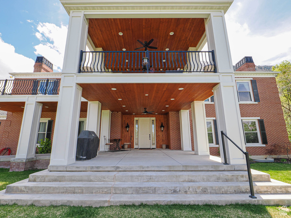 Doorway to property with a balcony, a ceiling fan, and brick siding