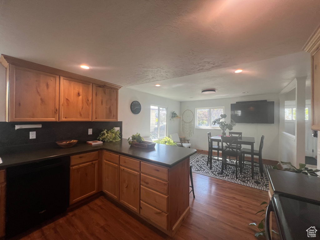 Kitchen with dark wood-style floors, dark countertops, a peninsula, and black dishwasher