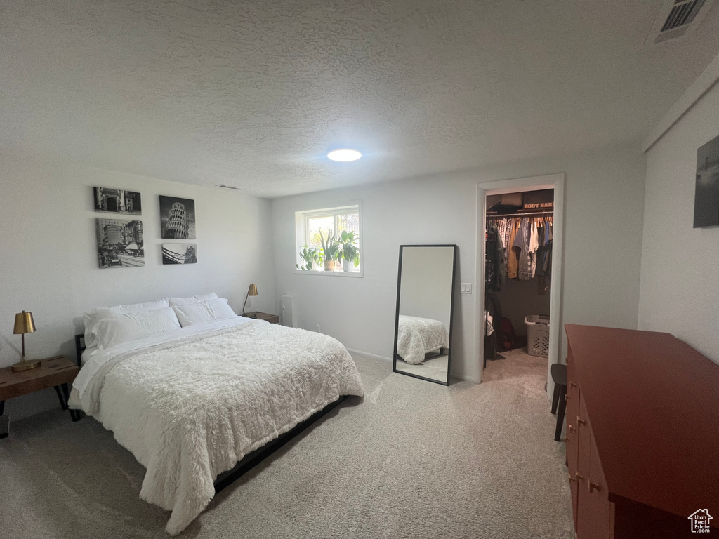 Bedroom featuring a closet, visible vents, light carpet, a textured ceiling, and a spacious closet