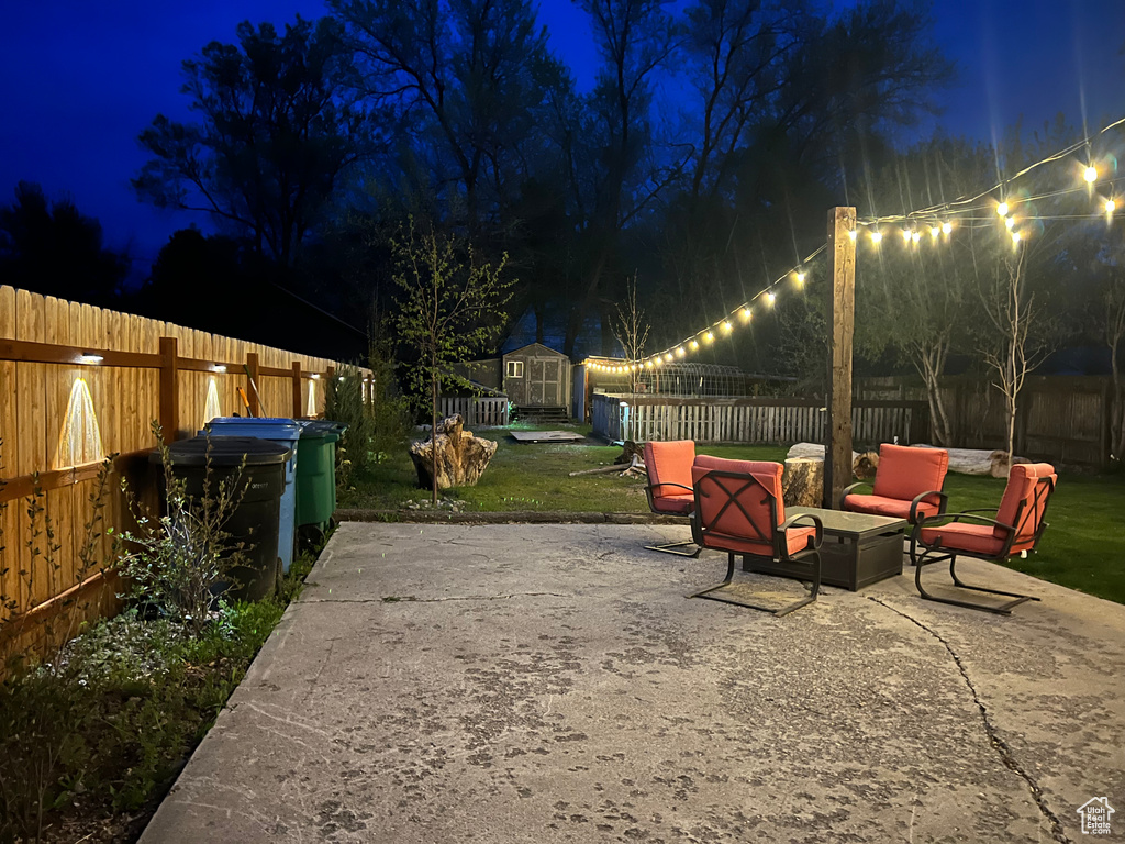 Patio at twilight with an outdoor structure, a fenced backyard, a shed, and an outdoor hangout area