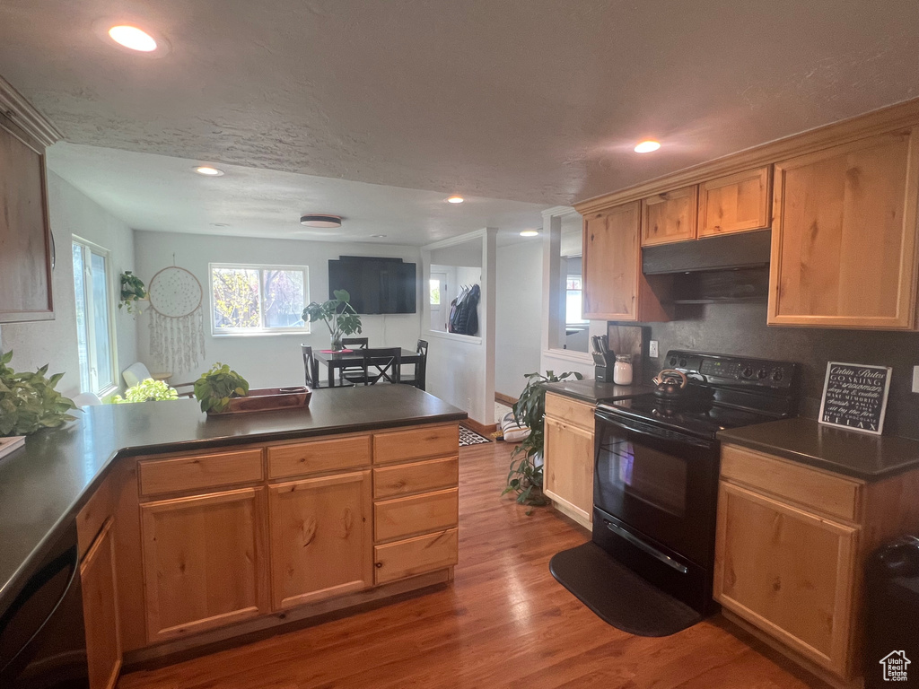 Kitchen with dark countertops, under cabinet range hood, black electric range, wood finished floors, and a peninsula