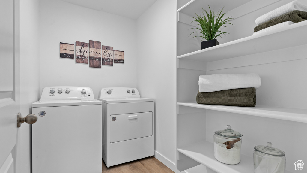 Clothes washing area with washer and dryer, laundry area, and light wood-style floors
