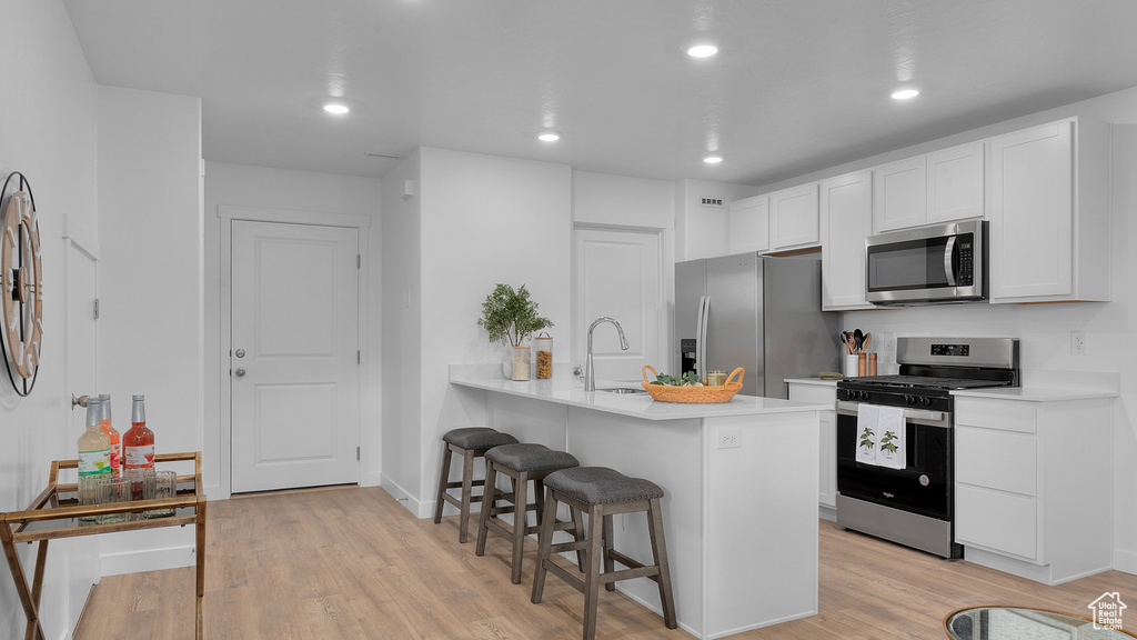 Kitchen featuring a kitchen bar, stainless steel appliances, light wood-style flooring, and a sink