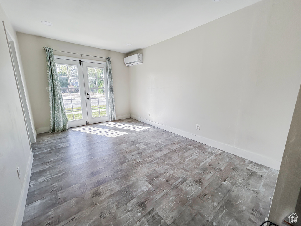 Empty room featuring a wall mounted air conditioner, wood finished floors, french doors, and baseboards