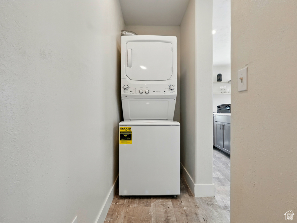 Clothes washing area with stacked washing machine and dryer, light wood-type flooring, and baseboards
