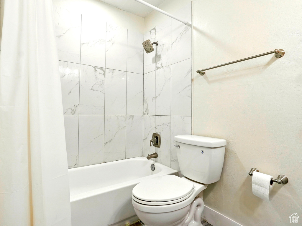 Bathroom with toilet, shower / tub combo, and baseboards
