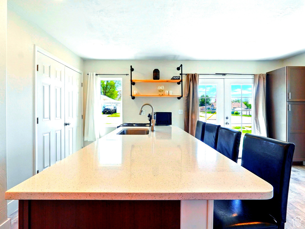 Kitchen with a sink, french doors, light stone counters, open shelves, and light wood finished floors