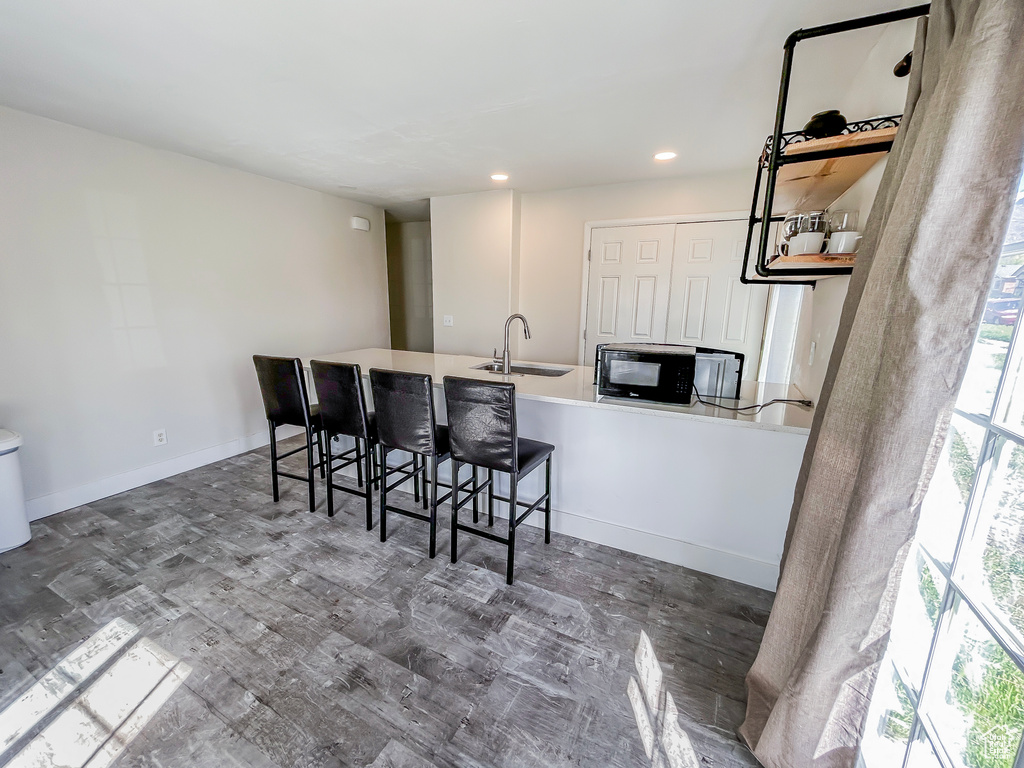 Kitchen featuring recessed lighting, wood finished floors, a kitchen bar, a sink, and black microwave