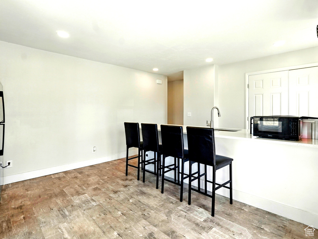 Kitchen featuring black microwave, a sink, wood finished floors, recessed lighting, and a breakfast bar area