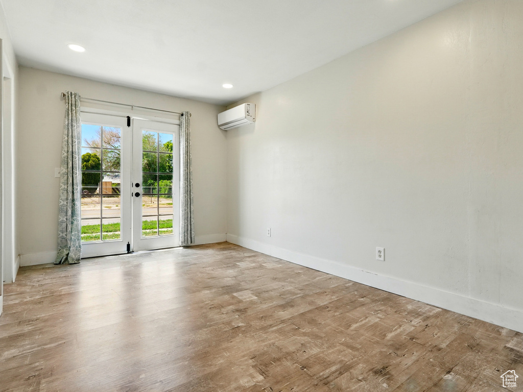Unfurnished room with a wall mounted AC, wood finished floors, baseboards, french doors, and recessed lighting