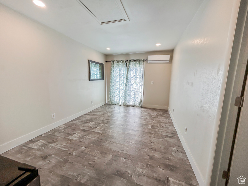 Unfurnished room with wood finished floors, a wall unit AC, recessed lighting, and baseboards