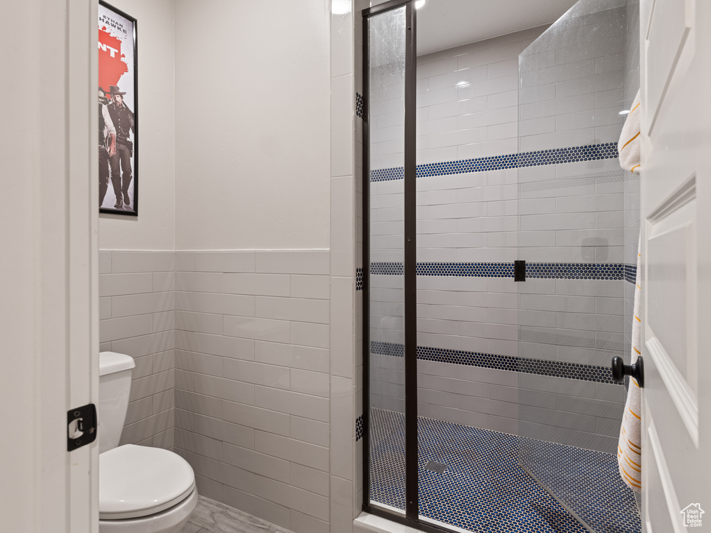 Full bath with tile walls, wainscoting, a shower stall, and toilet